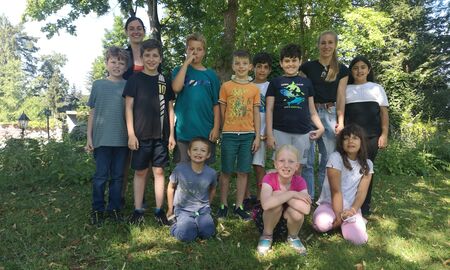 2 Lehrerinnen posieren mit 3 Schülerinnen und 7 Schülern für ein Gruppenfoto auf einer Wiese unter einem Baum