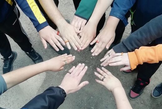 Schülerhände strecken sich zur Mitte entgegen, jeder trägt einen Ring.