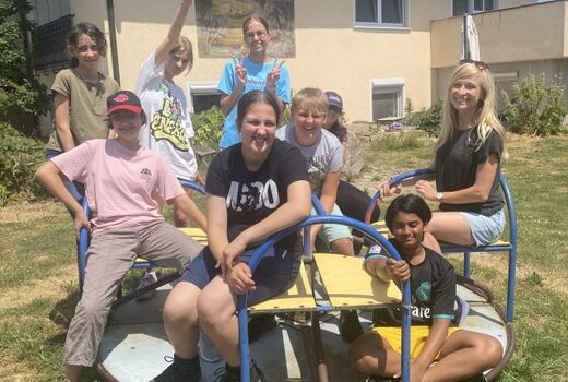 Acht SchülerInnen sitzen auf einem kleinen Kinderkarussell und schauen fröhlich Richtung Kamera.