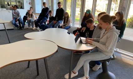 Jugendliche sitzen auf Hockern und hören aufmerksam zu