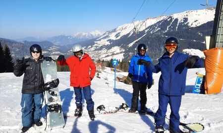 Vier Jugendliche posieren mit ihrem Snowboards im Schnee, im Hintergrund eine verschneite Gebirgslandschaft