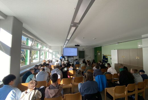 Ein großer Raum, in dem viele Schüler sitzen. Vorne hält ein Mitarbeiter des THW einen Vortrag.