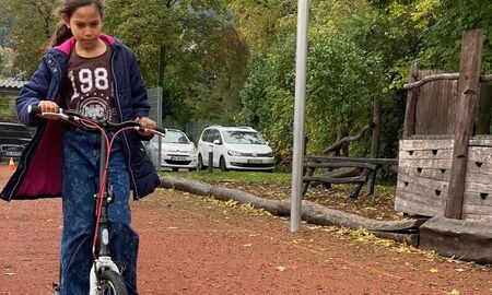 ein Mädchen fährt mit dem Roller zwischen zwei Holzleisten