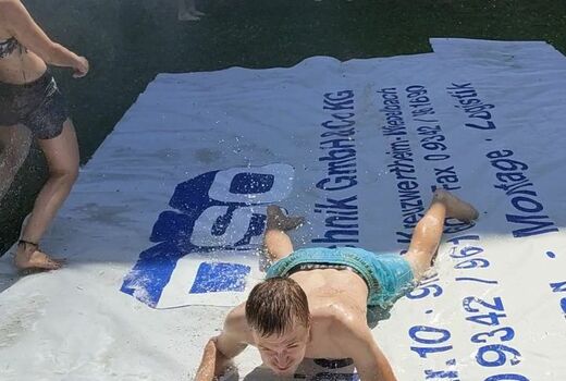 Ein großer Junge rutscht bäuchlings eine nasse LKW-Plane herunter.