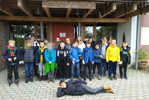 Alle Schülerinnen und Schüler der Klassen 4a und 4b stehen vor einem Hauseingang und ein Schüler liegt posierend vor allen auf dem Boden.