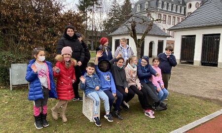 Neun junge Kinder und vier Jungendliche stehen oder sitzen auf der neuen Bank