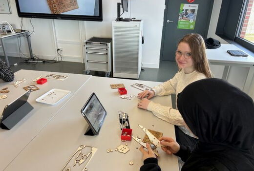 Eine Schülerin lächelt in die Kamera, vor ihr der Tisch mit Werkzeug und Bauteilen.