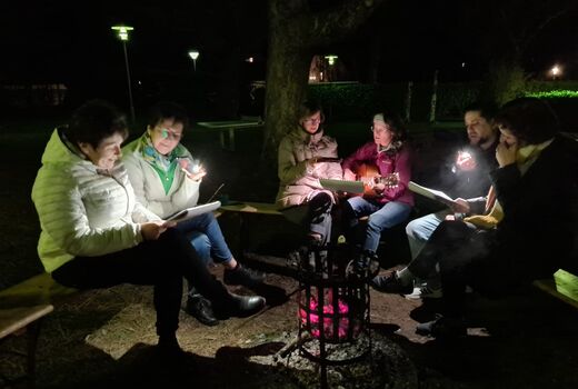 ErzieherInnen sitzen im Dunkeln um den Feuerkorb und musizieren.