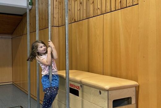 Ein Mädchen rutscht die Kletterstange in der Turnhalle herunter.