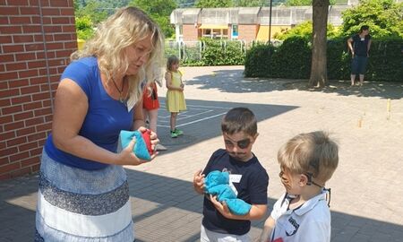 Eine Lehrerin erklärt zwei kleinen Jungen ein Spiel, bei dem Sandsäckchen in eine Lochplatte geworfen werden sollen.