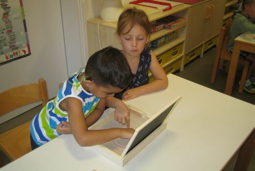 Zwei Kinder malen den Buchstaben O in den Sand.