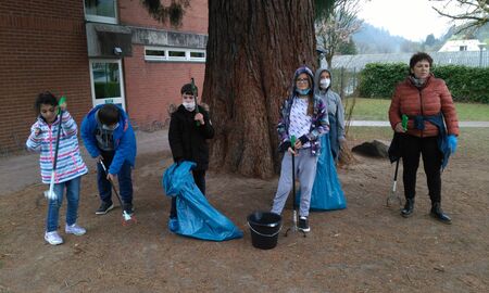 Schülerinnen, Schüler und eine Erzieherin stehen vor dem Mammutbaum. Sie halten Zangen und Tüten in der Hand.