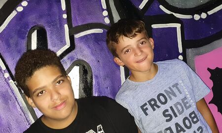 Zwei Jungen stehen nebeneinander vor dem Graffiti. Sie schauen beide in Richtung der Kamera.