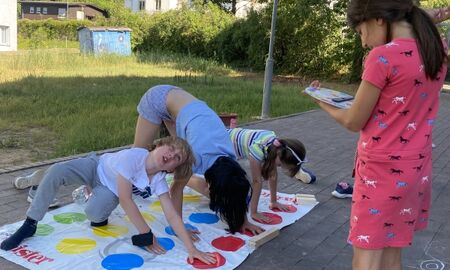 Vier Kinder Spielen gemeinsam ein Bewegungsspiel. Ein Kind liest etwas vor und drei Kinder berühren Farbpunkte auf einem Bodenteppich