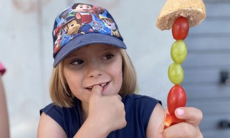 Ein Mädchen zeigt einen Gemüsespieß mit Trauben, Tomaten und einem Stück Baguette oben auf