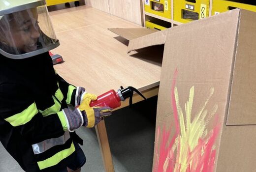 Ein Junge löscht mit einem Spielzeugfeuerlöscher ein aufgemaltes Feuer.