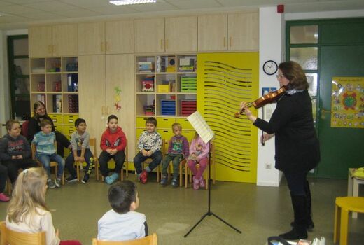 Eine Frau spielt Geige und Kinder hören ihr zu.