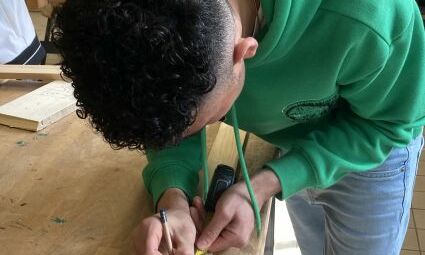 Ein junger Mann zeichnet eine Markierung auf ein Stück Holz