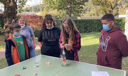 Eine Schülerin stapelt Streichhölzer auf einer Tischtennisplatte, andere Mitschüler und Mitschülerinnen schauen ihr aufmerksam zu.