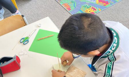 Ein Erstklässler steht seitlich an seinem Tisch, auf dem verschiedene Utensilien liegen, und baut sein Wasserfahrzeug.