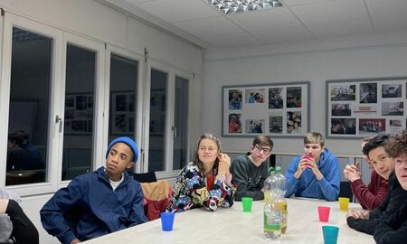 Jugendliche sitzen an einem langen Tisch und hören aufmerksam zu