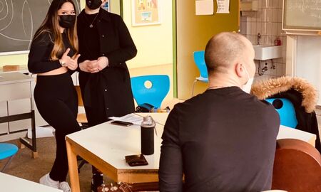 Zwei Mädchen singen, im Vordergrund sitzt ein junger Mann an der Gitarre