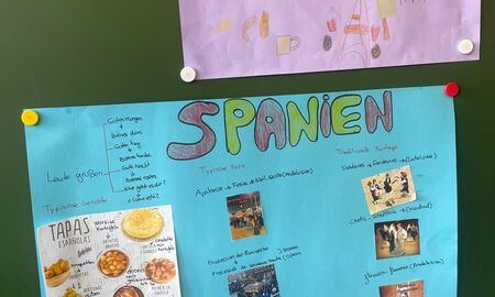 An der Tafel hängen zwei Plakate: Unten ein blaues Plakat über Spanien. Oben ein fliederfarbenes Plakat über Frankreich.