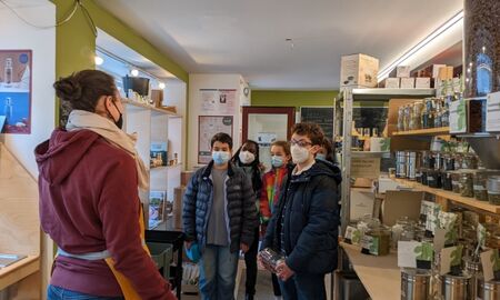 Fünf Kinder stehen im Unverpacktladen, eine Frau im Vordergrund scheint etwas zu erklären