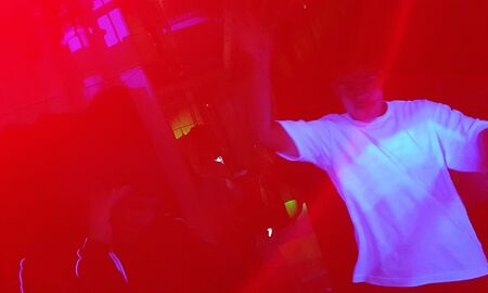 Zu sehen sind rote Lichteffekte und ein Junge im weißen T-Shirt. Er tanzt.