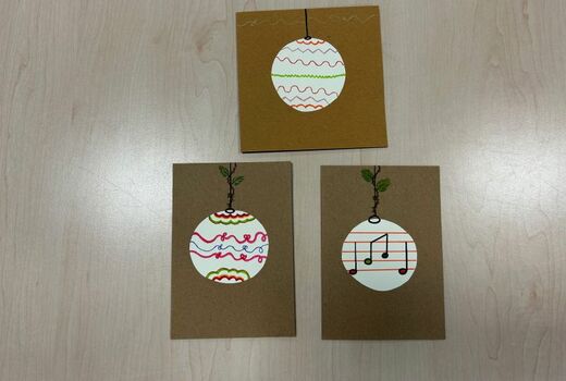Drei Weihnachtskarten aus braunem Karton. Im Zentrum jeweils eine Weihnachtskugel, die aus Papier ausgeschnitten und bunt bemalt wurde.