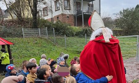 Eine Gruppe von Kindern steht im Halbkreis um den Nikolaus herum und ein Kind umarmt ihn als Dankeschön.