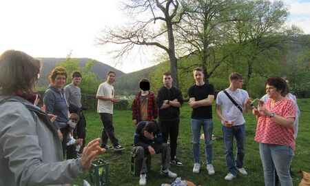 SchülerInnen bekommen die Aufgaben von einer Erzieherin erklärt. Alle stehen auf einer Wiese.