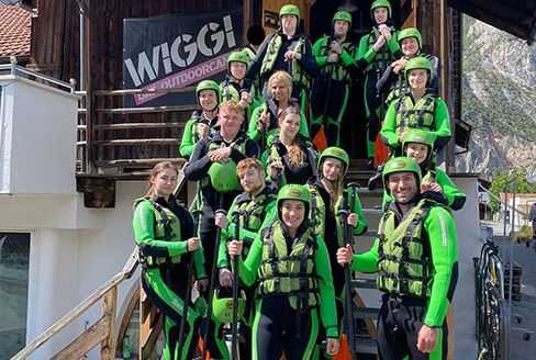 in Gruppenfoto in voller Ausrüstung mit Neopren, Schwimmwesten, Helm und Paddeln das kurz vor der Raftingtour aufgenommen wurde.