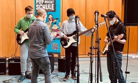 Drei Schüler üben mit einem Mitglied der Popakademie E-Gitarre