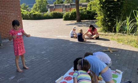Vier Kinder Spielen gemeinsam ein Bewegungsspiel. Ein Kind liest etwas vor und drei Kinder berühren Farbpunkte auf einem Bodenteppich