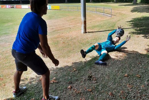 Zwei Personen üben Ball abwehren. Der Torwart liegt auf dem Boden und ist kurz davor, den Ball zu fangen.