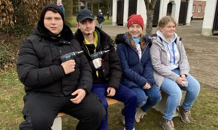 Vier Jungendliche sitzen auf der neuen Bank. Zwei davon halten Akkuschrauber vor ihre Brust
