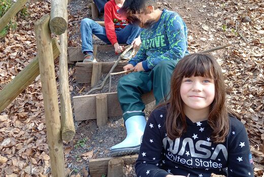 Kinder sitzen auf Stufen hintereinander und bearbeiten Stöcke