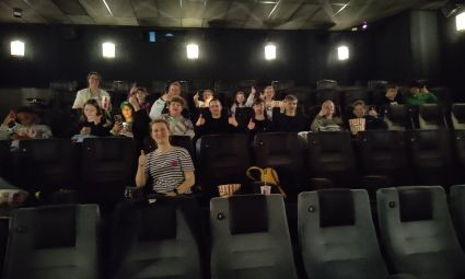 Viele Jugendliche sitzen gemeinsam in einem Kinosaal. Die Vorstellung hat noch nicht begonnen.