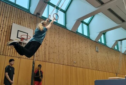 In einer Turnhalle schwingt eine Person an den Ringen.