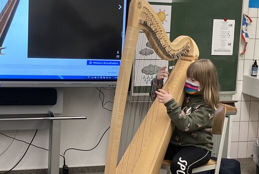 Eine Zweitklässlerin sitzt vorne vor der Tafel und zupft probeweise an einer Harfe.