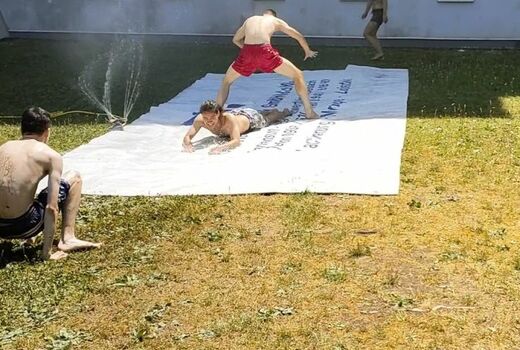 Zwei Personen rutschen die nasse LKW-Plane herunter, einer zwischen den Beinen des anderen hindurch.