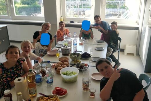 Acht SchülerInnen und eine Lehrerin sitzen um einen großen Abendessenstisch.
