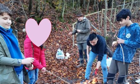 Schülerinnen und Schüler stehen um eine Feuerstelle herum und stochern im Feuer mit einem Stock