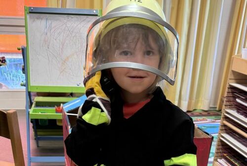 Ein Junge steht in Feuerwehrkleidung vor dem selbstgebastelten Feuerwehrauto.