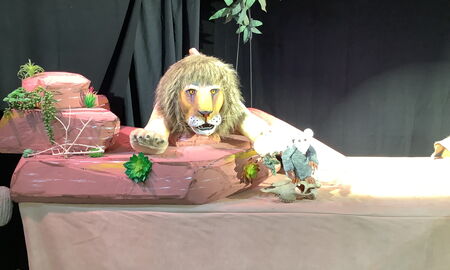 Auf einem Tisch liegen die Hauptfiguren des Theaterstücks, der Löwe und die Maus.