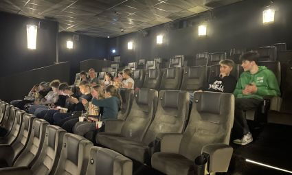 Viele Jugendliche sitzen gemeinsam in einem Kinosaal. Die Vorstellung hat noch nicht begonnen.