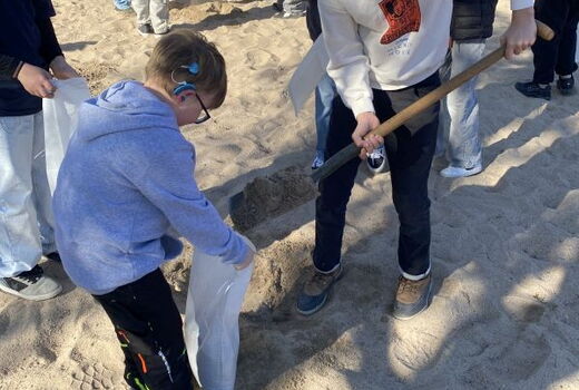Ein Schüler hält einen Sack, ein anderer befüllt ihr mit Sand