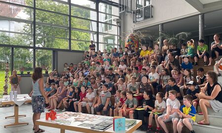 Die Schülerinnen und Schüler und erwachsenen Aufsichtspersonen sitzen im Publikum und hören gespannt zu.