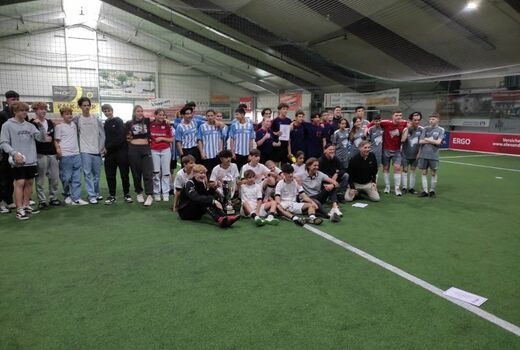 Gruppenfoto mit ca. 40 jugendlichen Teilnehmern des Turniers in der Fußballhalle. Ein Teil der Fußballer steht, ein Teil sitzt auf dem Rasen.